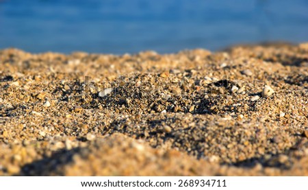 Blurred background image of sea sand and sun. Blurred picture with: partly visible texture of small stones and sand seashore lit by light rays of the evening sun. Beach, seashore. Support of the text.