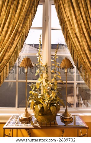 Interior view of window with curtains pulled back and decorative table with lamps and plant.