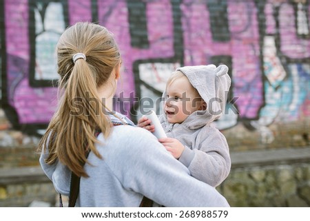mother holding baby with a mobile phone outdoors. 