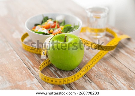 healthy eating, dieting, slimming and weigh loss concept - close up of green apple, measuring tape and salad Royalty-Free Stock Photo #268998233