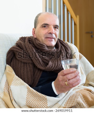 Mature male with scarf, blanket and dissolving medicine in glass at home 