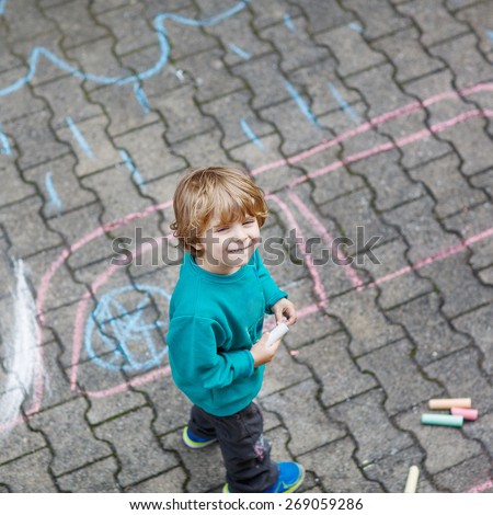 Happy little blond kid boy painting with colorful chalks outdoors in summer. Kid having fun. Creative leisure with children outdoors.