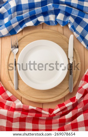 plate, knife and fork at cutting board on wooden background