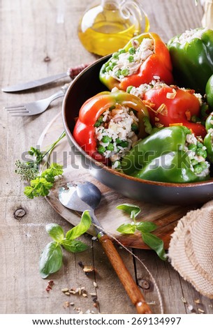 Colorful bell peppers stuffed with rice and peas, herbs and oil on rustic wooden background closeup. Selective focus, shallow depth of field