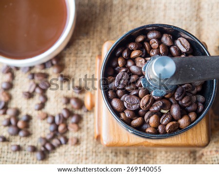 The roasted coffee beans in a coffee grinder with blur coffee beans and fresh coffee  on sack background.