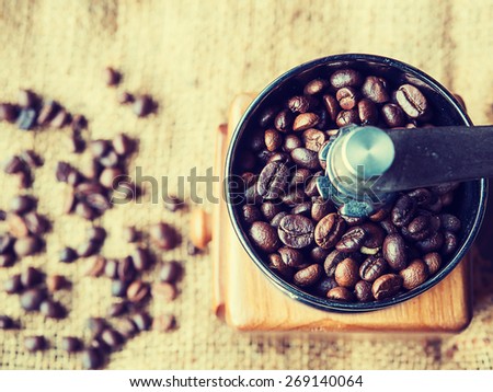 Vintage style photo of the roasted coffee beans in a coffee grinder with blur coffee beans on sack background.
