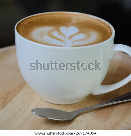 a cup of latte art on wooden plate