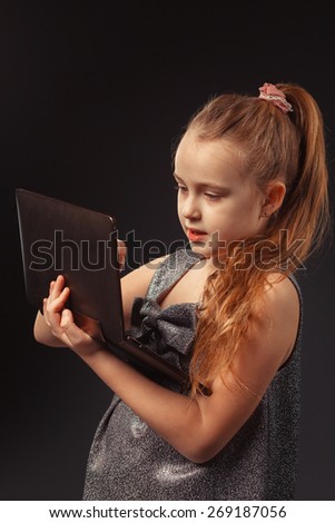 education, free time, technology and internet concept - little student girl with tablet pc on a dark background