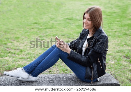 Cool pretty woman with the mobile sitting on a bank at the park