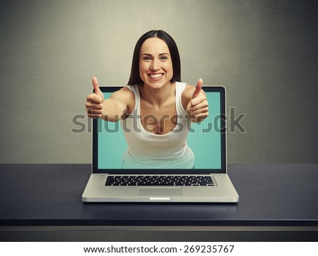 smiley woman stretching out of laptop and showing thumbs up against dark background