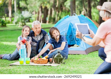 Grandmother photographing family through digital tablet at campsite