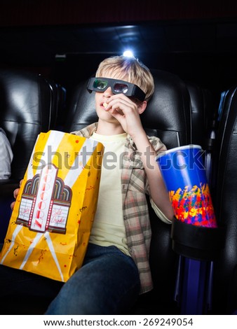 Boy eating popcorn while watching 3D movie in cinema theater
