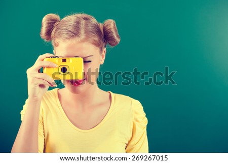 Portrait of student girl holding photo camera in front of blackboard, intentionally toned