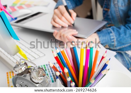 young woman artist in jeans jacket drawing something on graphic tablet at the office