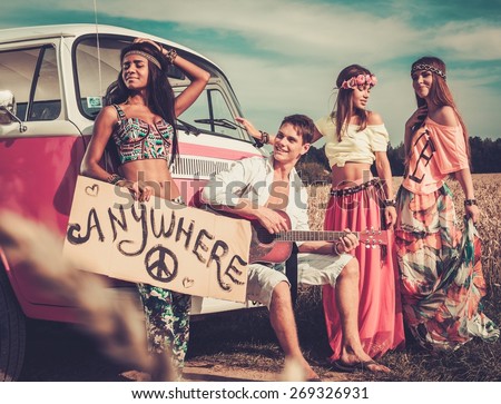 Multinational hippie hitchhikers with guitar and luggage on a road Royalty-Free Stock Photo #269326931