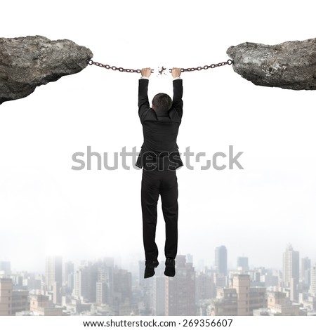 Businessman hand hanging on the broken rusty iron chains connect two cliffs with urban scene skyline background