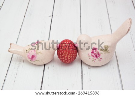 Two vintage ceramic birds holding an easter egg on a white wooden background