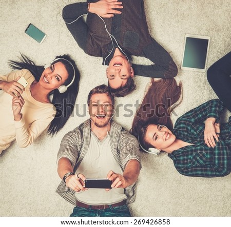 Happy multiracial friends relaxing on a carpet with gadgets 