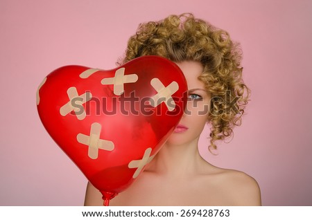 upset woman with ball in shape of heart on pink background