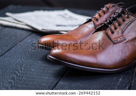 A pair of brown leather shoes with vintage camera and newspaper on a black wooden floor Royalty-Free Stock Photo #269442152