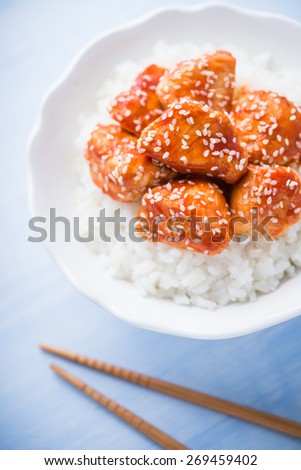 Spicy sweet and sour chicken with sesame and rice on blue wooden background close up. Oriental food.