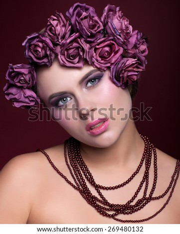 Portrait of beautiful young woman with artificial rouses on head necklace on red marsala color background