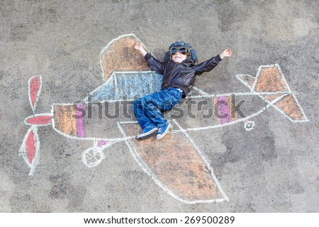Happy little kid boy in pilot uniform having fun with airplane picture drawing with colorful chalk. Creative leisure for children outdoors in summer. Royalty-Free Stock Photo #269500289