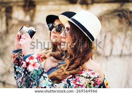 Outdoor lifestyle portrait of two best friends hipsters making photo on their vintage camera, having fun together, joy and happiness, wearing trendy bright clothes caps and sunglasses.