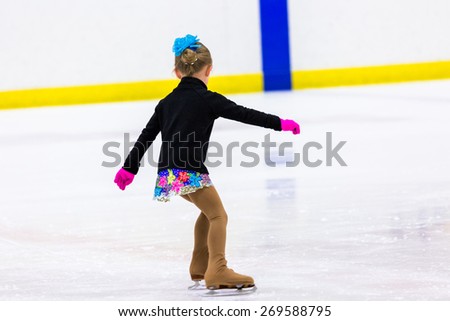 Young figure skater practicing at indoor skating rink.