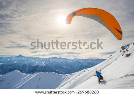 Paraglider running on snowy slope for take off with bright orange kite. Stunning background of the italian Alps in winter season. Shot taken in backlight, unrecognizable person. Royalty-Free Stock Photo #269688260