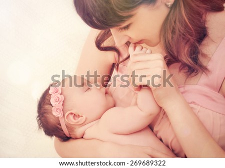 caring mother kissing little fingers of her cute sleeping baby girl, happy family concept