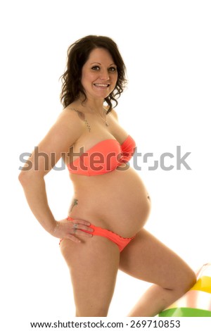 a pregnant woman in her peach bikini holding onto her beach ball with a tattoo on her shoulder.