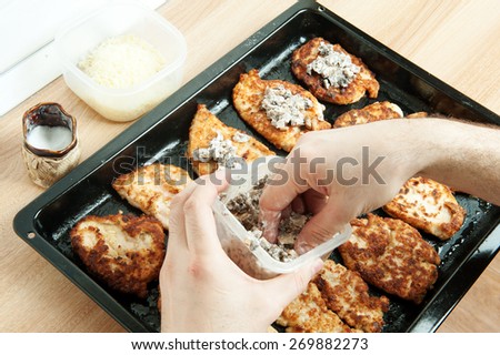 grilled chicken breast. meat is laid on a black pan, poured with sauce and melted cheese. Cooking meat at home in the oven.