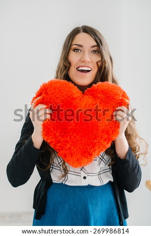 Picture of a big red heart in hands, female holds handmade sewn soft toy, woman with Valentine gift against the window, happy girl smiling, conceptual image of health care or love.