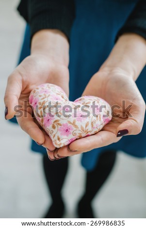 Picture of a small white heart in hands, female holds handmade sewn soft toy, woman with Valentine gift against the window, happy girl smiling, conceptual image of health care or love.