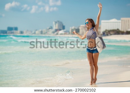 Woman on a tropical beach with beach bag. fit young woman with stripy bag at tropical beach. beautiful girl walking the summer beach
