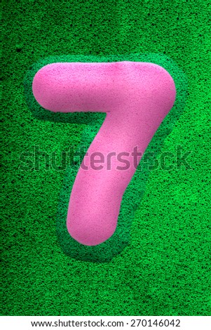 The number seven in a pink sponge like texture, raised 3D from the green background.