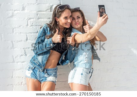 two girls friends taking selfie together wearing jeans jackets and shorts summer jeanswear street urban casual style having fun