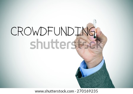 closeup of the hand of a young caucasian man in a grey suit writing the word crowdfunding in the foreground, slight vignette added