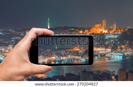 Male hand with smartphone taking a picture of Istanbul at night. Tourism concept.