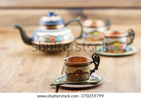 Traditional Turkish tea set: vintage painted copper cups with teapot on wooden table. Focus on the front cup
