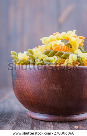 Raw pasta in wooden bowl on wood background - process old dark style picture