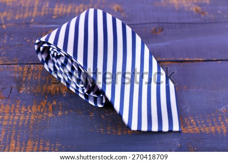 Rolled striped tie on wooden background