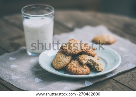 Homemade oat and nut cookies and glass of milk on wooden table. Toned picture