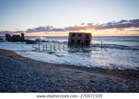 waves crushing over rocks and ruins of old fort at sunset on the beach