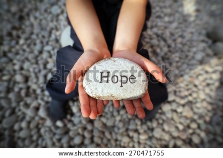 Child on a beach with hands cupped holding stone pebble with the word hope engraved concept for faith, love, spirituality and religion