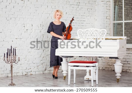young woman in black dress playing violin against white interior Studio