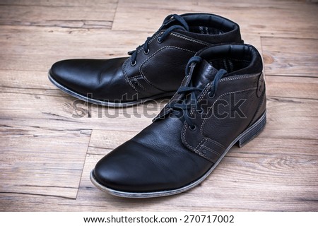 A pair of men's black leather ankle shoes placed on wooden floor