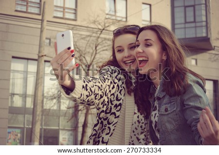 Photo in vintage style. Two girls taking pictures of themselves and laughing at city background.