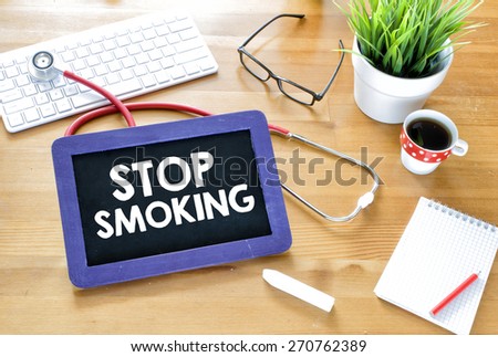 Stop smoking on blackboard.  Handwritten stop smoking with chalk on blackboard,stethoscope, keyboard,notebook,glasses,cup of coffee and green plant on wooden background